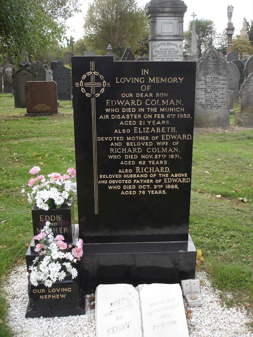 A black granite headstone with gold lettering in a cemetery, with flowers in front