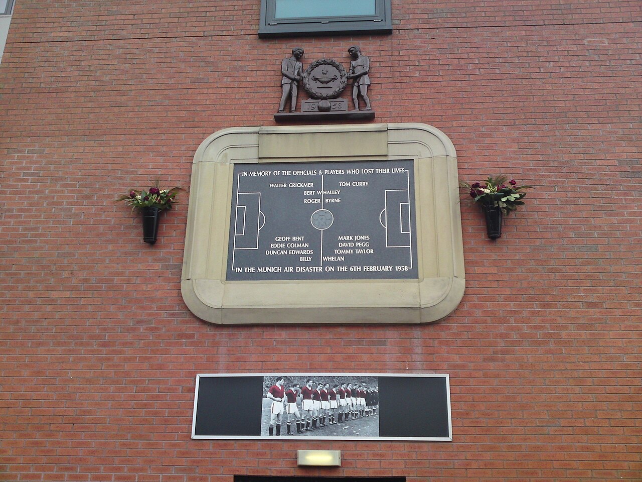 A stone plaque laid out like a football pitch with names inscribed, set into a red-brick wall